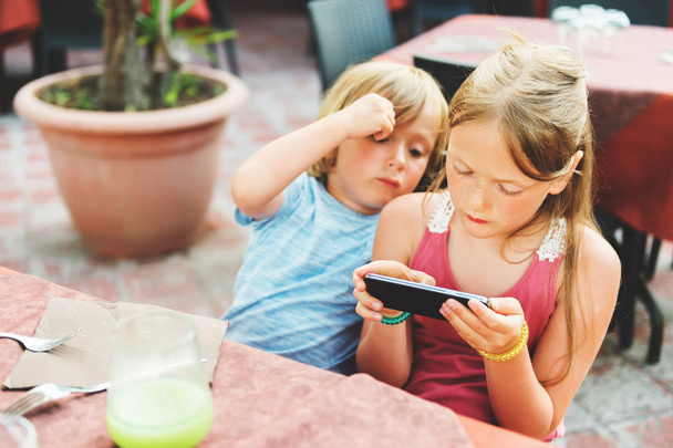 Two kids playing electronic games on the phone while waiting food orders in restaurant - Φωτογραφία, εικόνα