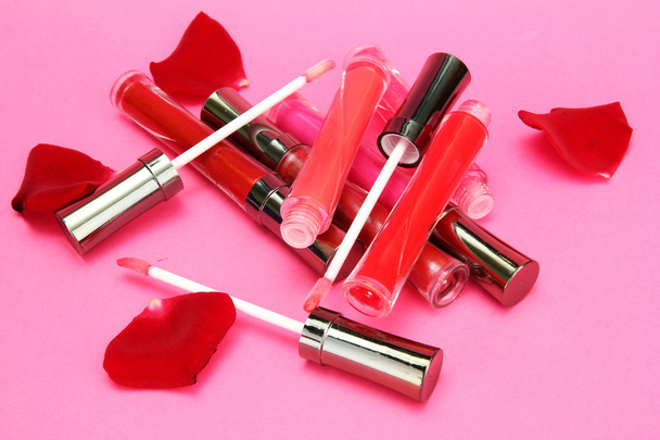 beautiful lip glosses with rose petals, on pink background - Fotó, kép