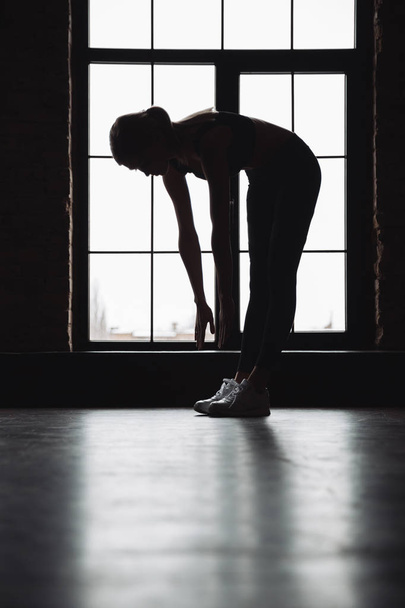 Silhouette of fitness woman stretching near the window - Zdjęcie, obraz