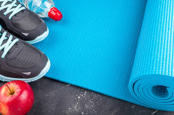 Yogamatte, Sportschuhe, Äpfel, Wasserflasche auf dunklem Hintergrund. Konzept gesunder Lebensstil, gesunde Ernährung, Sport und Ernährung. Sportgeräte - Foto, Bild
