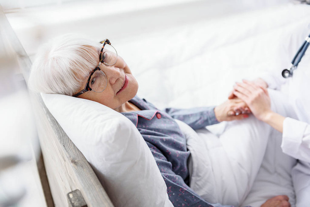 Cheerful old woman situating in cot in hospital - Foto, afbeelding