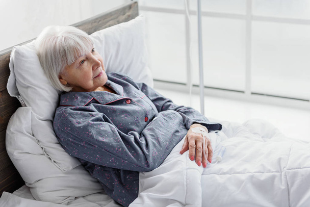 Glad retiree is on drip flask reclining in bed - Valokuva, kuva