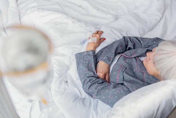 Спокійний пенсіонер на крапельниці, що сидить у ліжку
 - Фото, зображення