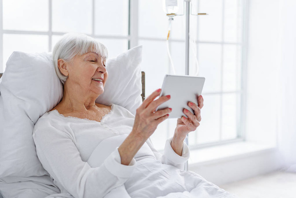 Smiling retiree looking at digital tablet in clinic - Fotó, kép