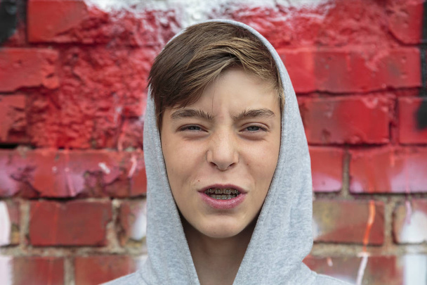 adolescente enojado con aparato ortopédico y pared roja
 - Foto, Imagen