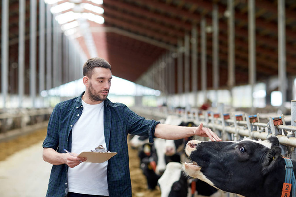 farmer with clipboard and cows in cowshed on farm - Photo, Image