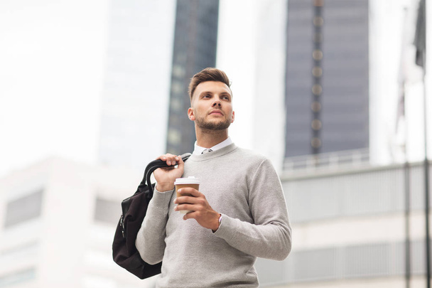 young man with bag drinking coffee in city - Фото, зображення
