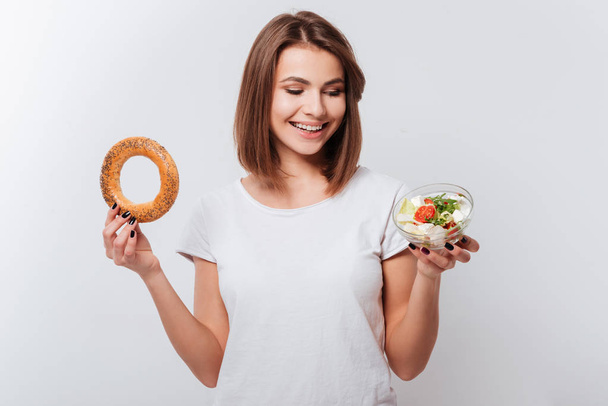 Hungry young woman holding bagel and salad - Foto, immagini