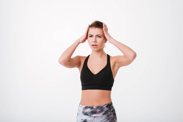 Confused young fitness lady holding head with hands - Foto, afbeelding