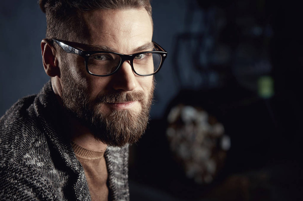 Closeup portrait of handsome smiling young man with beard in glasses on dark background - Foto, Imagen