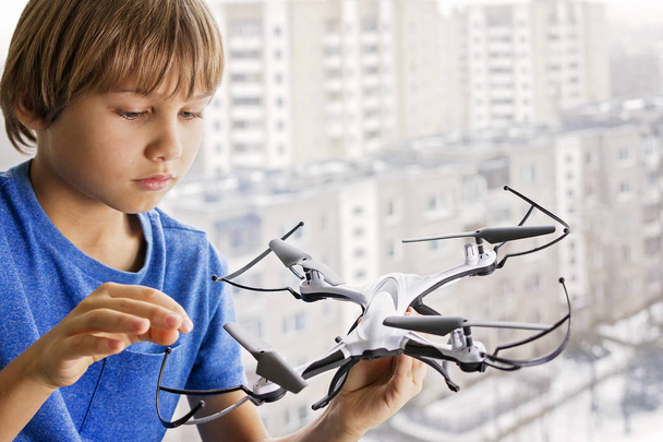 Child playing with drone. Boy near the window holding quadrocopter in his hand. Technology, leisure toys concept - Фото, изображение
