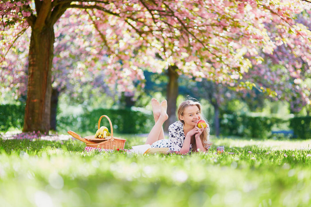 Beautiful young woman having picnic in blooming spring park - Valokuva, kuva