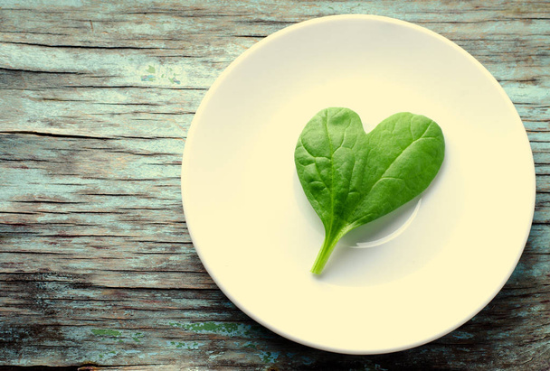Fresh Baby spinach heart shape leaf on white plate, blue wooden background. Top view with copy space. Love, Healthy, Ecology concept - Φωτογραφία, εικόνα