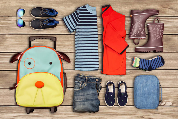 Lasten matkatavaraluettelo (vaatteet ja kengät) puulattialle asetettuna
 - Valokuva, kuva