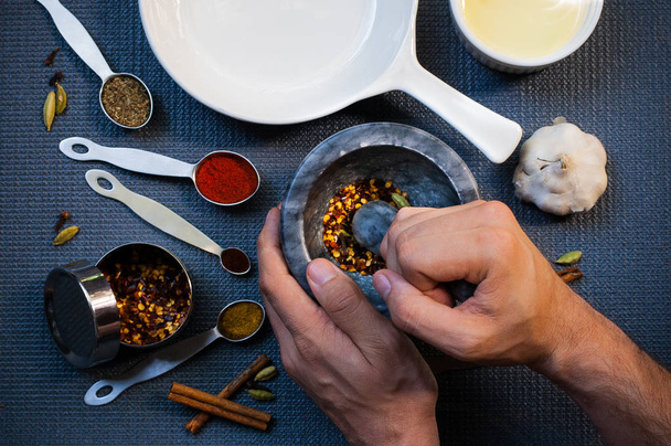 One man grinding spices in a granite mortar on a kitchen table with various kitchen equipment on it - Photo, Image