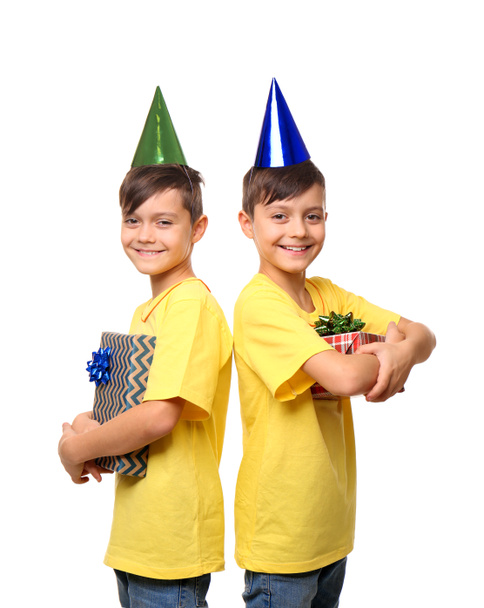 Lindos niños gemelos con sombreros de cumpleaños y regalos sobre fondo blanco
 - Foto, Imagen