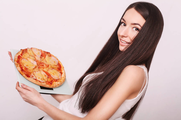 Δίαιτα. Όμορφη κοπέλα ζύγιση κλίμακας κρατώντας πίτσα. Η έννοια της υγιεινής διατροφής και της παχυσαρκίας. Το κορίτσι όμορφη λεπτή σιλουέτα. Ανθυγιεινών τροφίμων. Τρόπος ζωής. Απώλεια βάρους. Η παχυσαρκία - Φωτογραφία, εικόνα