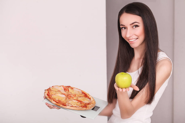 Dieta. Jovem mulher bonita faz uma escolha entre estilo de vida saudável e alimentos nocivos. O conceito de alimentação saudável e obesidade. Menina bela figura esbelta
 - Foto, Imagem
