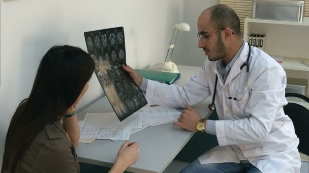 Male doctor showing brain computed tomography to female patient and filling in form - Video