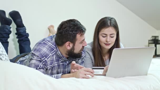 Ευτυχισμένο ζευγάρι χρησιμοποιώντας ένα φορητό υπολογιστή ξαπλωμένος σε ένα κρεβάτι στο σπίτι - Πλάνα, βίντεο