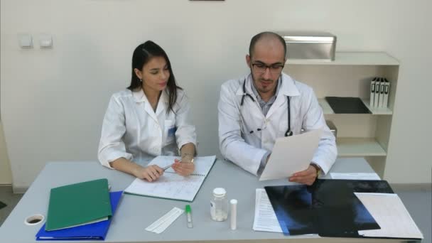 Doctor showing his female assistant how to read cardiogram while she making notes - Video