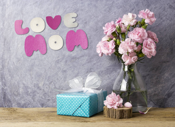 Moeders dag concept van liefde moeder brief pink carnation bloemen in fles en blauw Geschenkverpakking op oud hout - Foto, afbeelding