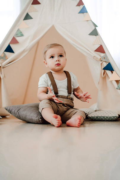 Portrait of lovely little boy happy smiling celebrating 1 year birthday. One year old european little gentleman sitting in a baby tent wigwam - Фото, изображение