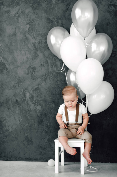 Portrait de charmant petit garçon heureux souriant célébrant 1 anniversaire. Un petit homme européen d'un an assis sur une chaise et jouant avec des ballons
 - Photo, image