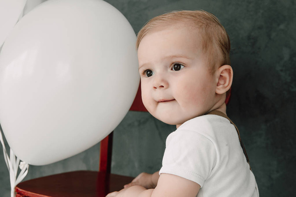 Porträt eines liebenswerten kleinen Jungen glücklich lächelnd, der 1 Jahr Geburtstag feiert. Ein Jahr alter europäischer kleiner Herr spielt mit Luftballons - Foto, Bild