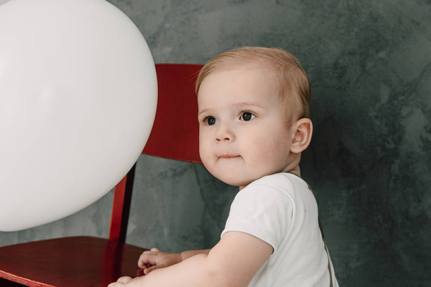 Retrato del adorable niño feliz sonriendo celebrando 1 año de cumpleaños. Un pequeño caballero europeo de un año jugando con globos
 - Foto, imagen