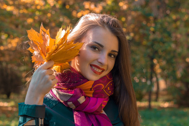 beautiful smiling girl with red lipstick holds in his hand leaves close-up - Фото, изображение