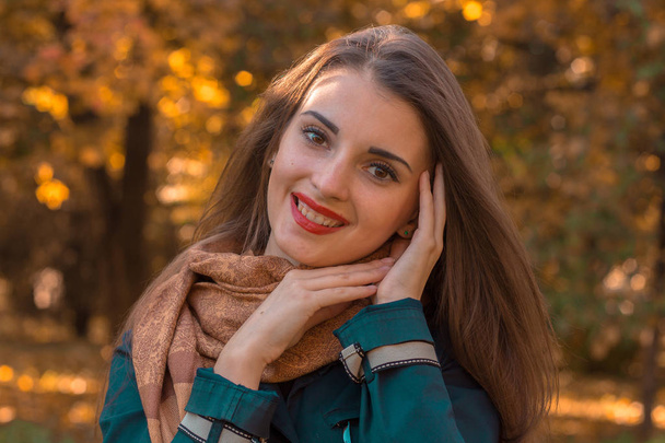 Portrait of a young smiling girl with red lipstick on lips which stands in the Park and keeps hands near facial close-up - Fotografie, Obrázek