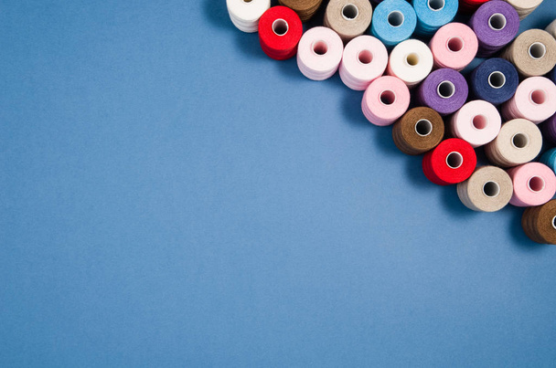 Top view of colorful thread spools over blue background - Foto, Imagem