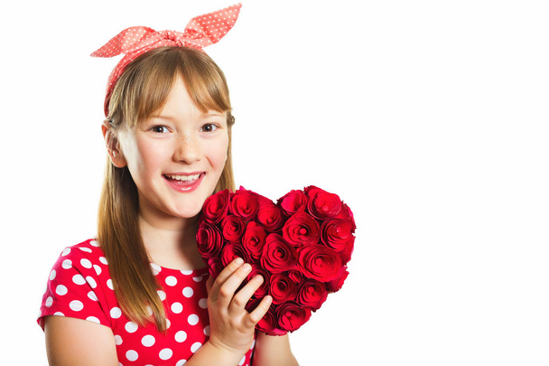 Studio shot of young little 9-10 year old girl, wearing red polka dot dress and headband, isolated on white background, pin up style, holding big decoration heart, Saint Valentine concept - Photo, Image