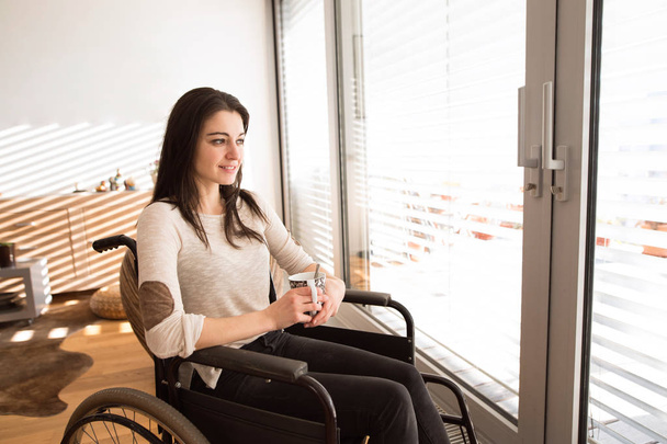 Beautiful young disabled woman in wheelchair at home. - Foto, afbeelding