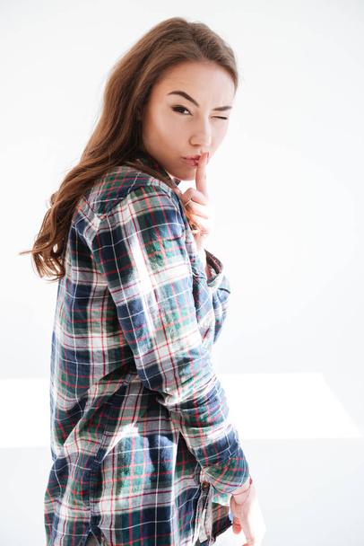 Attractive woman in plaid shirt showing silence sign and winking - Фото, изображение