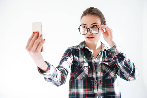 Woman looking over glasses and taking selfie with cell phone - Foto, Imagen