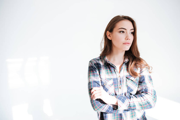 Thoughtful young woman in plaid shirt standing with arms crossed - Fotoğraf, Görsel