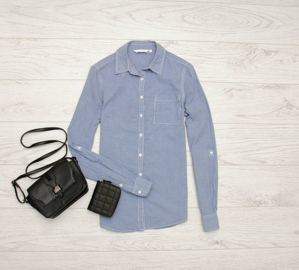 Синя сорочка в маленьких клітинах, чорна сумка, гаманець. Концепція моди. Вид зверху
 - Фото, зображення
