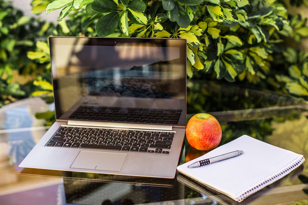 laptop on a green background. on a glass table has a laptop, a notebook with a pen and apple.the concept of work and healthy food outdoors - Valokuva, kuva