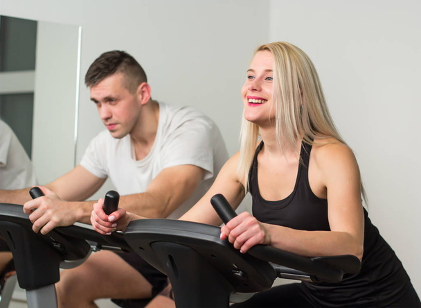 Mladý muž a žena na kole v tělocvičně, cvičení nohy dělat kardio cvičení spinningová kola - Fotografie, Obrázek