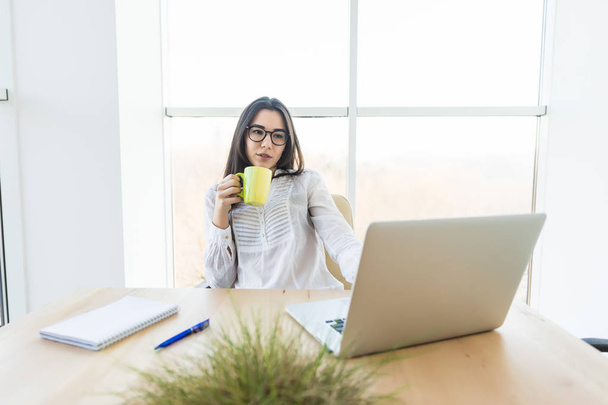 Молода бізнес леді п'є каву і дивиться на ноутбук в конференц-залі
 - Фото, зображення