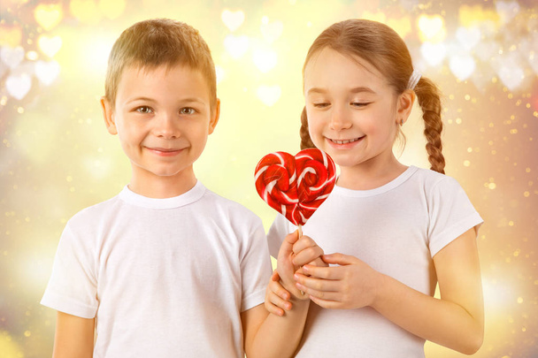 Junge schenkt einem kleinen Mädchen bonbonrote Lutscher in Herzform. Valentinstag. Kinder lieben. - Foto, Bild