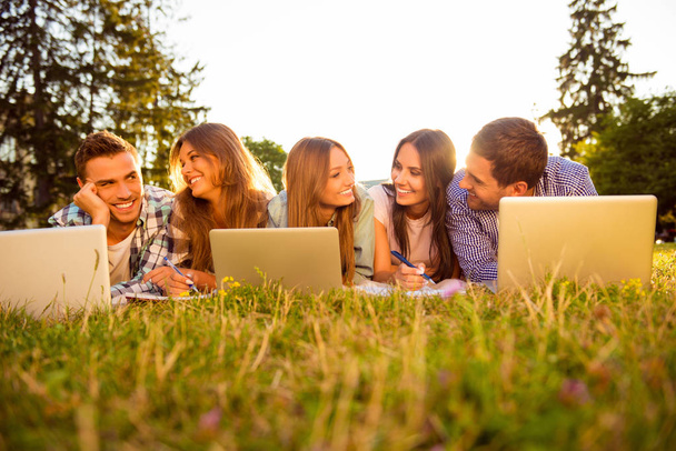 Five cheerful best friends lying on grass with laptops - Fotó, kép