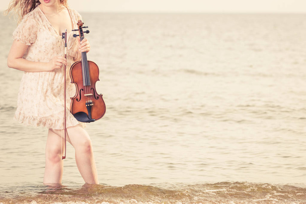Donna sulla spiaggia vicino al mare che tiene violino
 - Foto, immagini