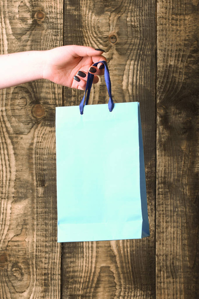 blue shopping bag in female hand on wooden background - Фото, зображення
