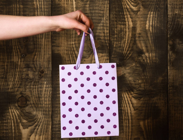 white spotted shopping bag in female hand on wooden background - Фото, зображення