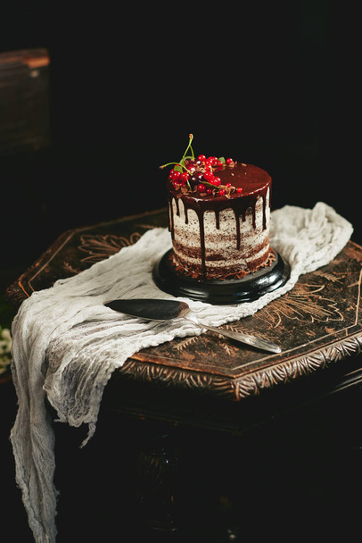 古い木製のテーブルに赤い果実カシスとチョコレートのケーキ - 写真・画像