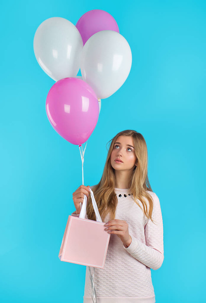 Sweet nice girl with baloons and little prersents bag in the hands on the blue background. Shopping and party mood. - Фото, зображення