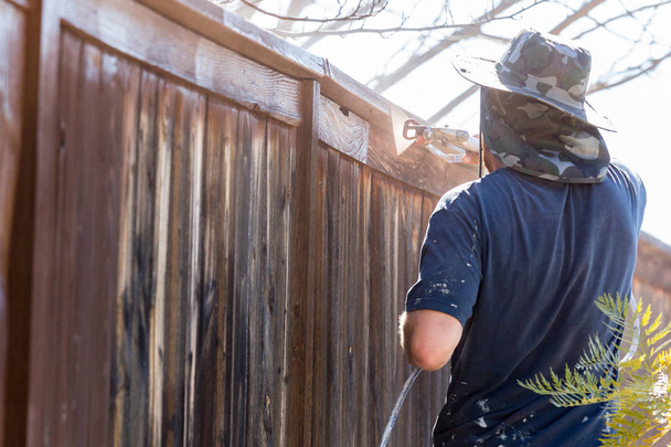 Professionele schilder huis tuin hek met hout vlek te spuiten. - Foto, afbeelding